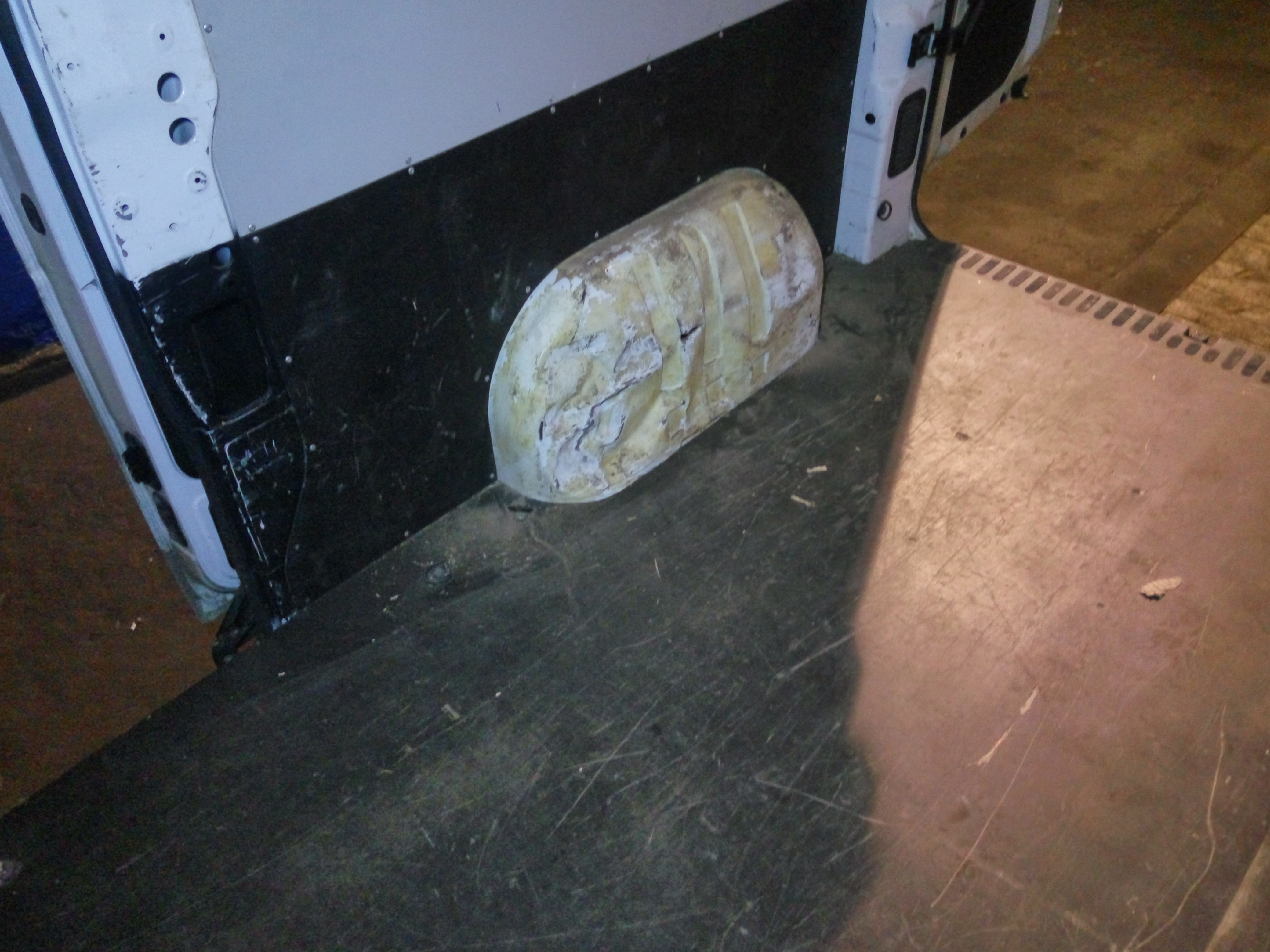 Wnętrze furgonetki w trakcie wygłuszania, widoczna czarna mata wygłuszająca na ścianie i element wygłuszający nadkole, zabezpieczony taśmą.