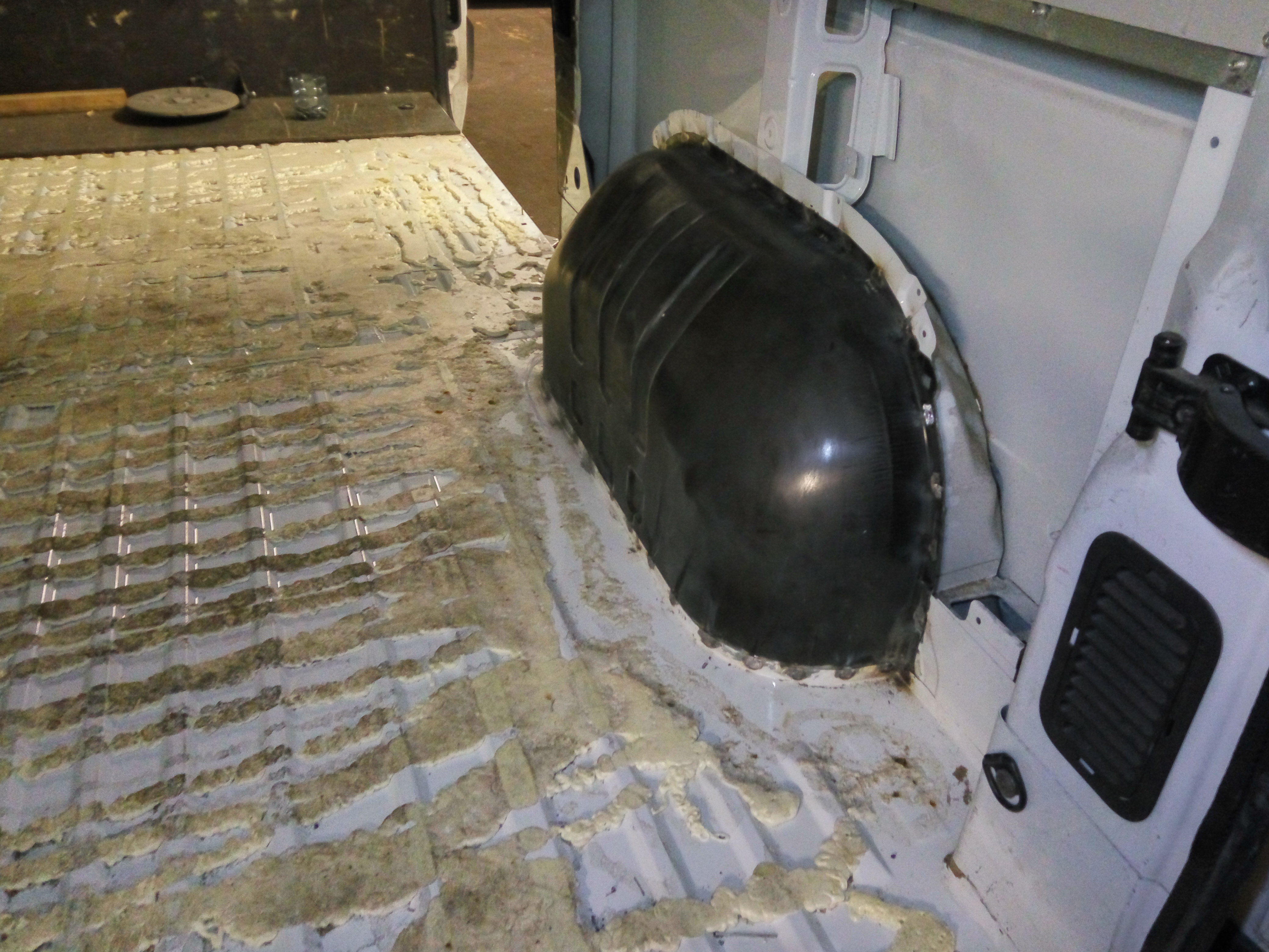 Wnętrze furgonetki w trakcie zabezpieczania antykorozyjnego, widoczna czarna nadkola oraz podłoga z naniesioną pianą uszczelniającą, przygotowana do dalszych prac.