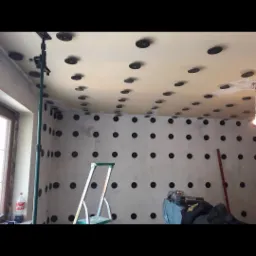 Wnętrze w trakcie montażu płyt kartonowo-gipsowych: widoczne profile mocujące na ścianach i suficie, drabina, narzędzia, butelka Coca-Coli przy oknie.