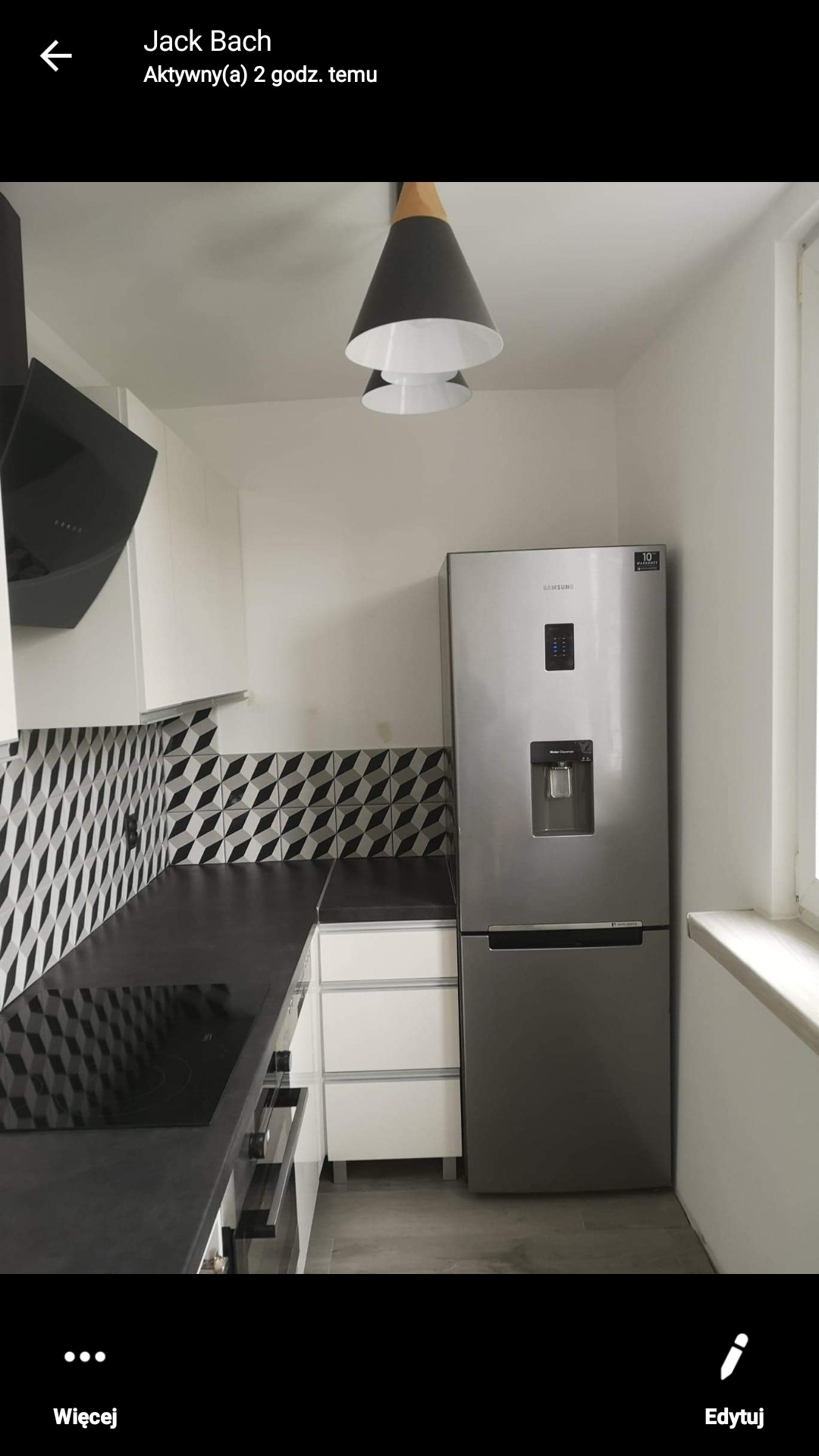 Nowoczesna kuchnia z czarnym blatem, geometrycznymi płytkami na ścianie, srebrną lodówką Samsung i designerskimi lampami wiszącymi w kształcie stożków.