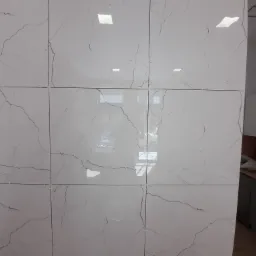 Ściana wyłożona błyszczącymi, białymi płytkami imitującymi marmur z widocznymi krzyżykami dystansowymi, odbicie okna i fragmentu ulicy w płytkach, sąsiadująca z zabudową kuchenną.