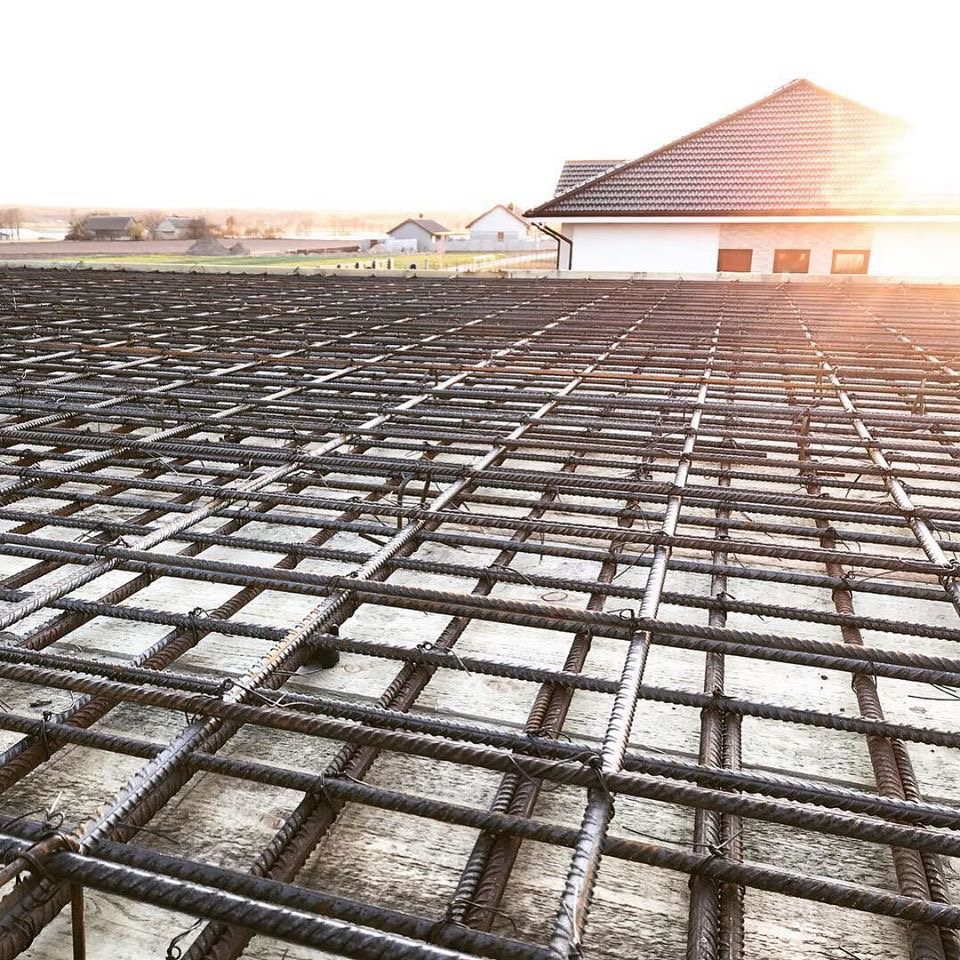 Siatka zbrojeniowa ułożona na szalunku pod wylewkę, widok z niskiej perspektywy w kierunku wschodzącego słońca, w tle zabudowa jednorodzinna.