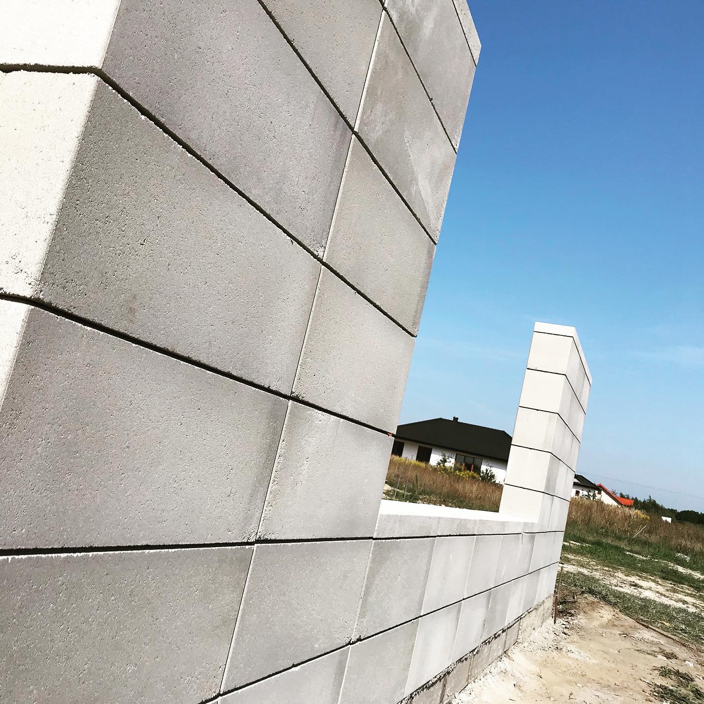 Wznoszone ściany domu z betonu komórkowego, widok przez otwór okienny na budynek w tle, błękitne niebo