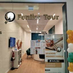 Feniks Tour Agnieszka Kozyra - Wejście do biura z logo Feniks Tour, dekoracja z balonów żółto-biało-zielonych, wewnątrz plakaty z ofertami wakacyjnymi i siedzenia dla klientów.