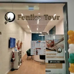 Wejście do biura z logo Feniks Tour, dekoracja z balonów żółto-biało-zielonych, wewnątrz plakaty z ofertami wakacyjnymi i siedzenia dla klientów.