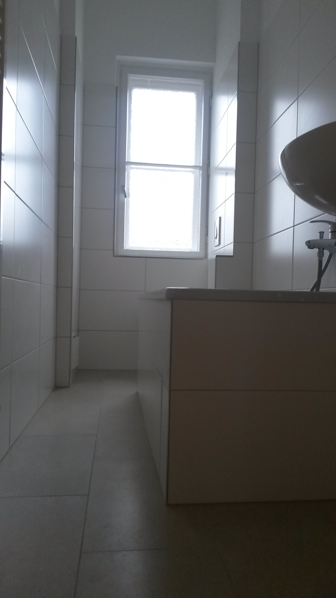 Wykończona łazienka w Zgorzelcu, z białymi płytkami na ścianach i podłodze, widok na okno i umywalkę z szafką.