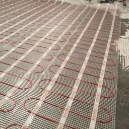 Jarosław Śmietana - Rozłożona mata grzewcza Warmtec z czerwonymi kablami na podłożu przygotowanym pod płytki, widoczne narzędzia glazurnicze w tle.