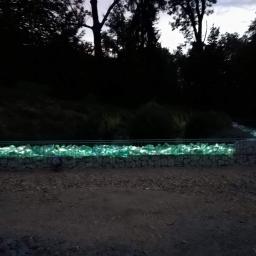 Jarosław Śmietana - Nocne ujęcie gabionu wypełnionego podświetlonymi, szklanymi bryłami, tworzące efektowną barierę w ogrodzie.