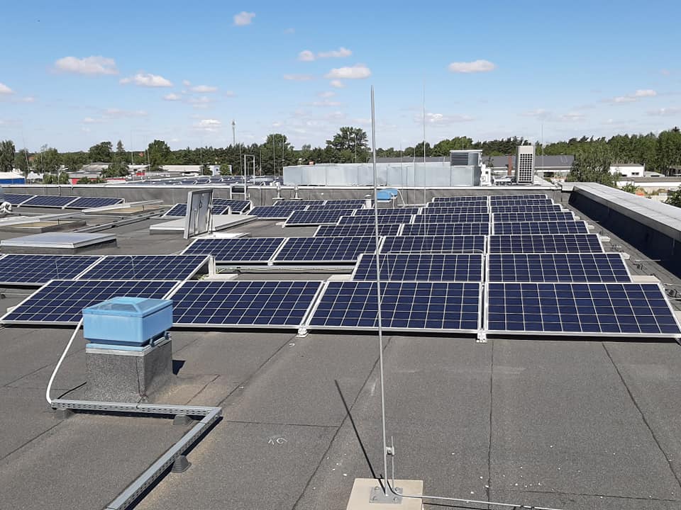 Rozległa instalacja paneli słonecznych na płaskim dachu budynku komercyjnego, widoczny system odgromowy i elementy wentylacyjne.