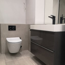 SUPRA PRZEDSIĘBIORSTWO BUDOWLANE - Nowoczesna łazienka z podwieszaną toaletą, czarnym panelem sterującym spłukiwaniem, szarą glazurą i szafką pod umywalką z czarną armaturą.