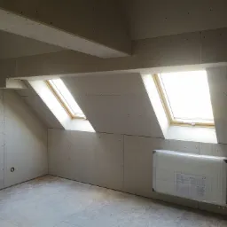 Poddasze z oknami dachowymi i grzejnikiem w folii, ściany i sufit wykończone płytami karton gips, widoczne łączenia płyt.