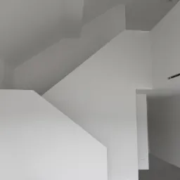 Minimalistyczne wnętrze z białymi ścianami, nietypowe załamania płaszczyzn, oświetlenie punktowe na suficie, surowy styl.