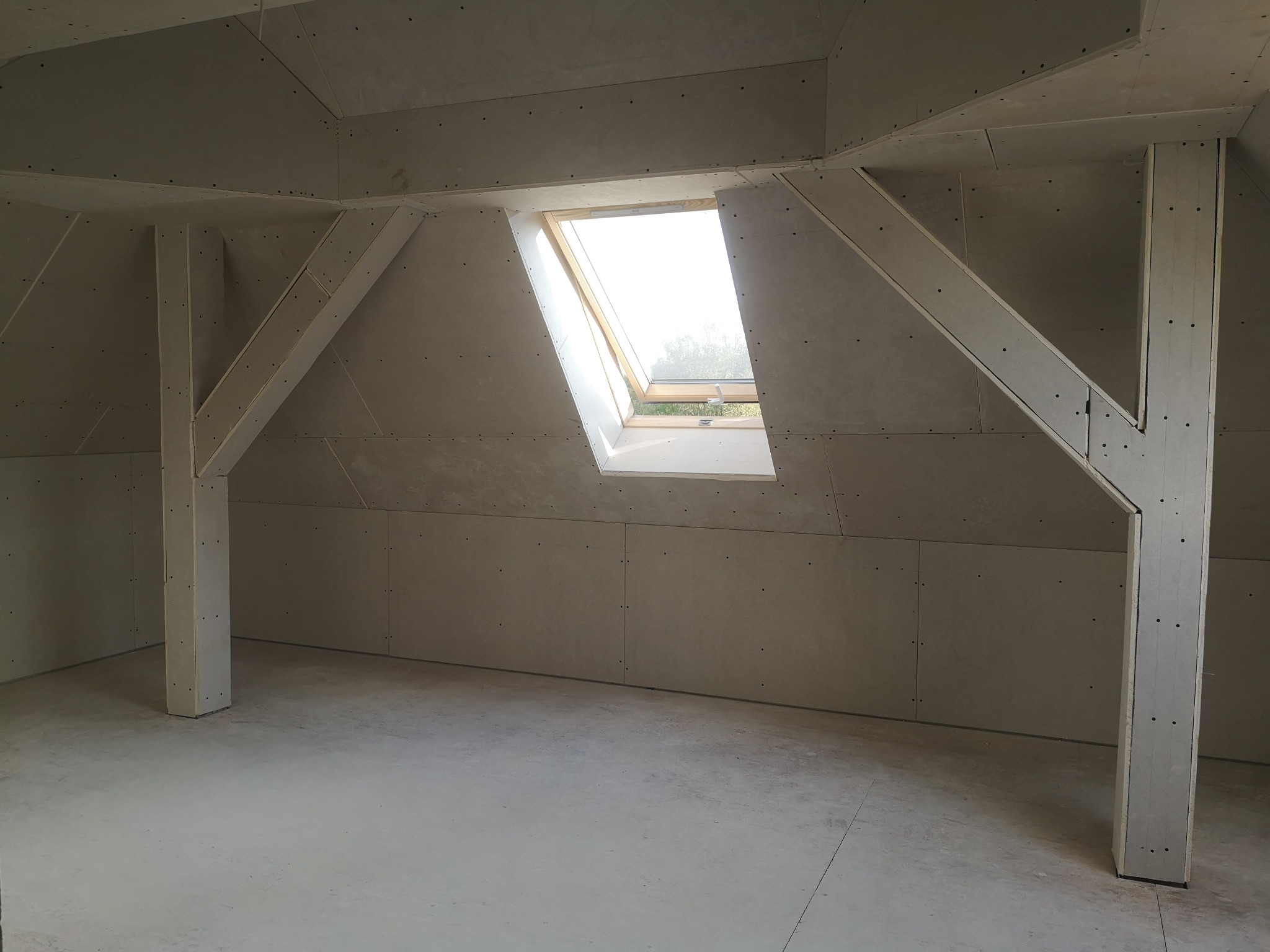 Poddasze z oknem dachowym, ściany wyłożone płytami gipsowo-kartonowymi na konstrukcji wsporczej, widoczne ślady po szpachlowaniu.