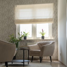 Między Myślami - Jasne wnętrze gabinetu z dwoma fotelami, stolikiem kawowym, kwiatami w wazonie i doniczkach na parapecie okna z roletą rzymską.