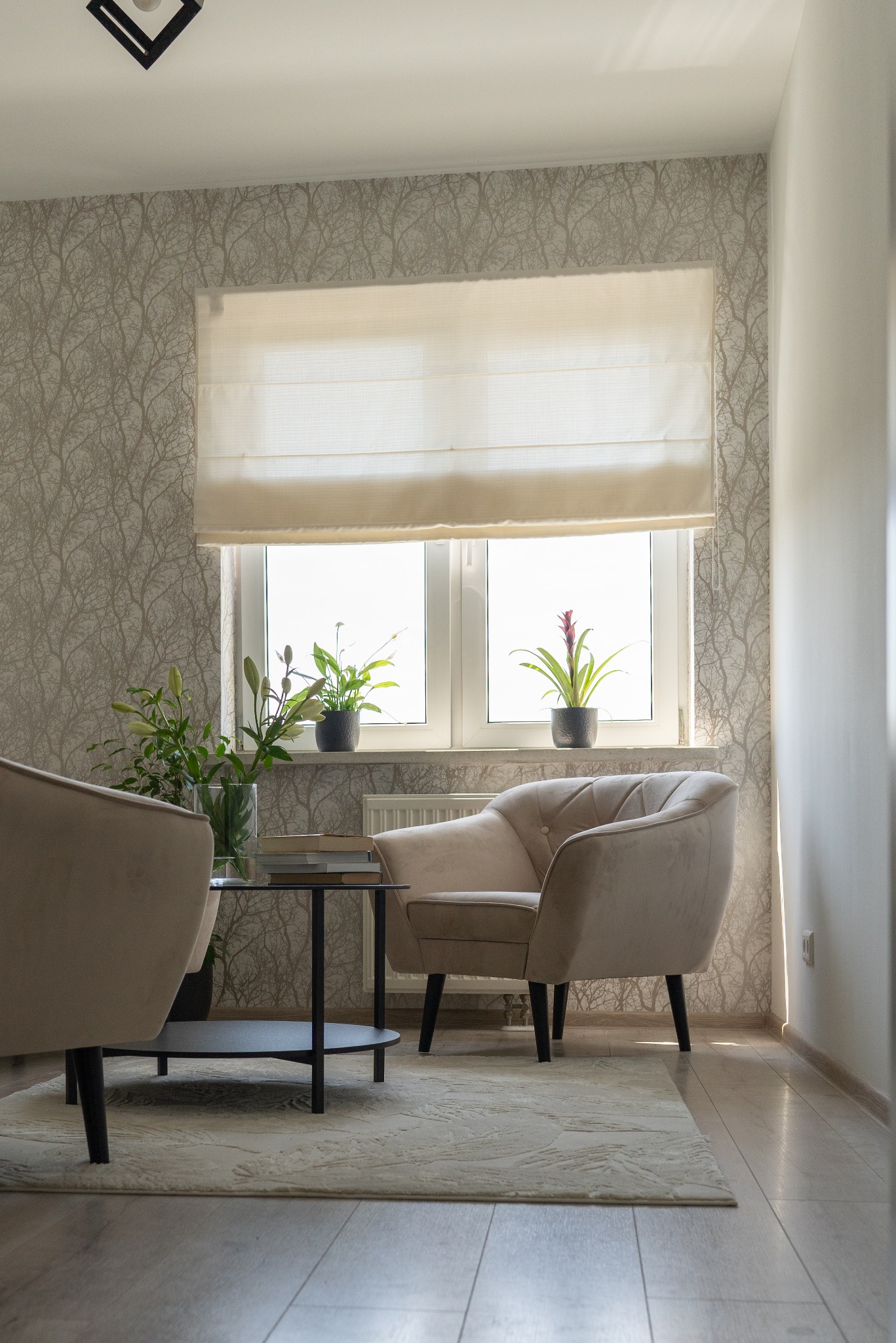 Jasne wnętrze gabinetu z dwoma fotelami, stolikiem kawowym, kwiatami w wazonie i doniczkach na parapecie okna z roletą rzymską.