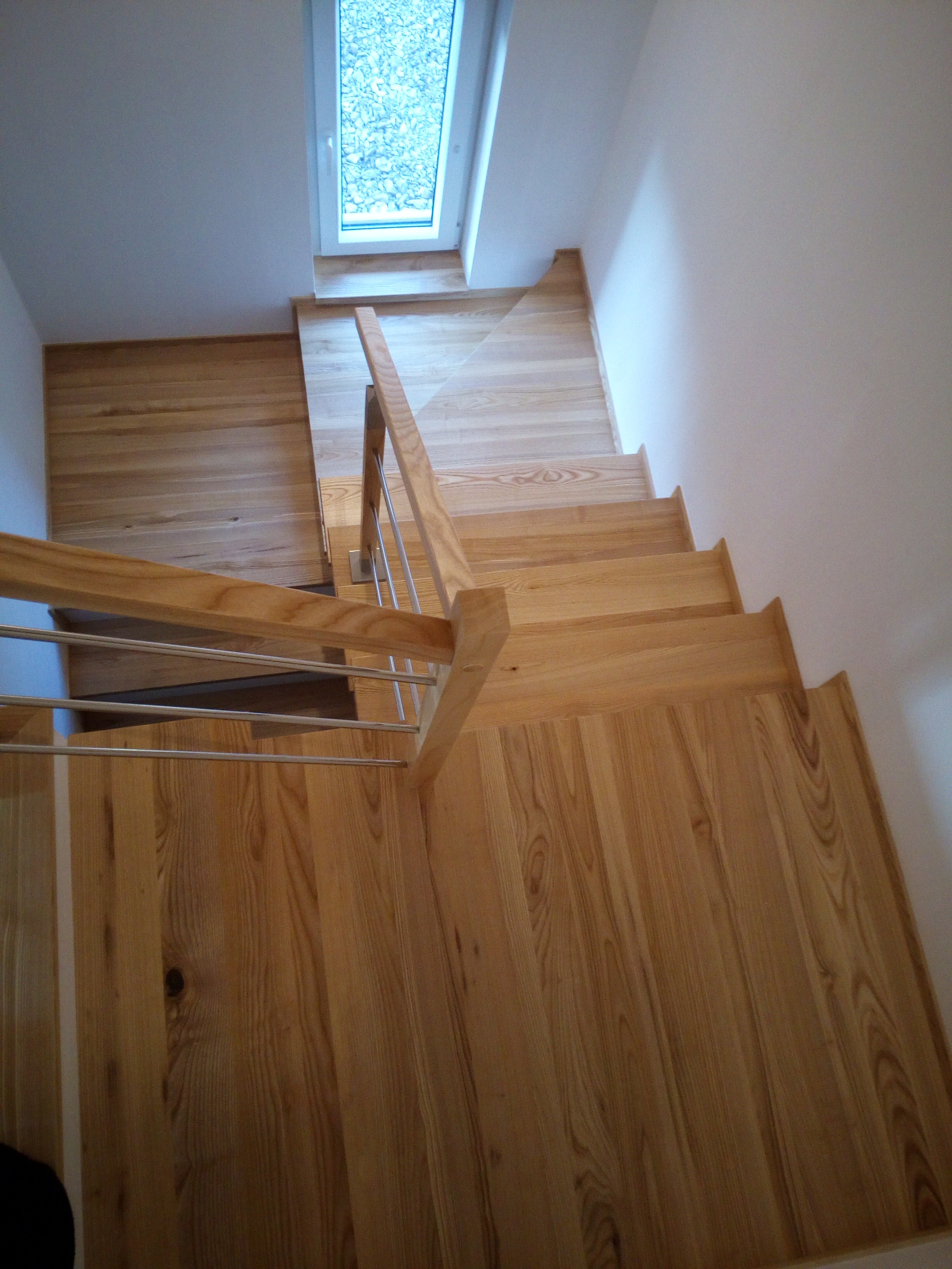 Jasne, drewniane schody z metalową balustradą i oknem na podeście, widok z góry.