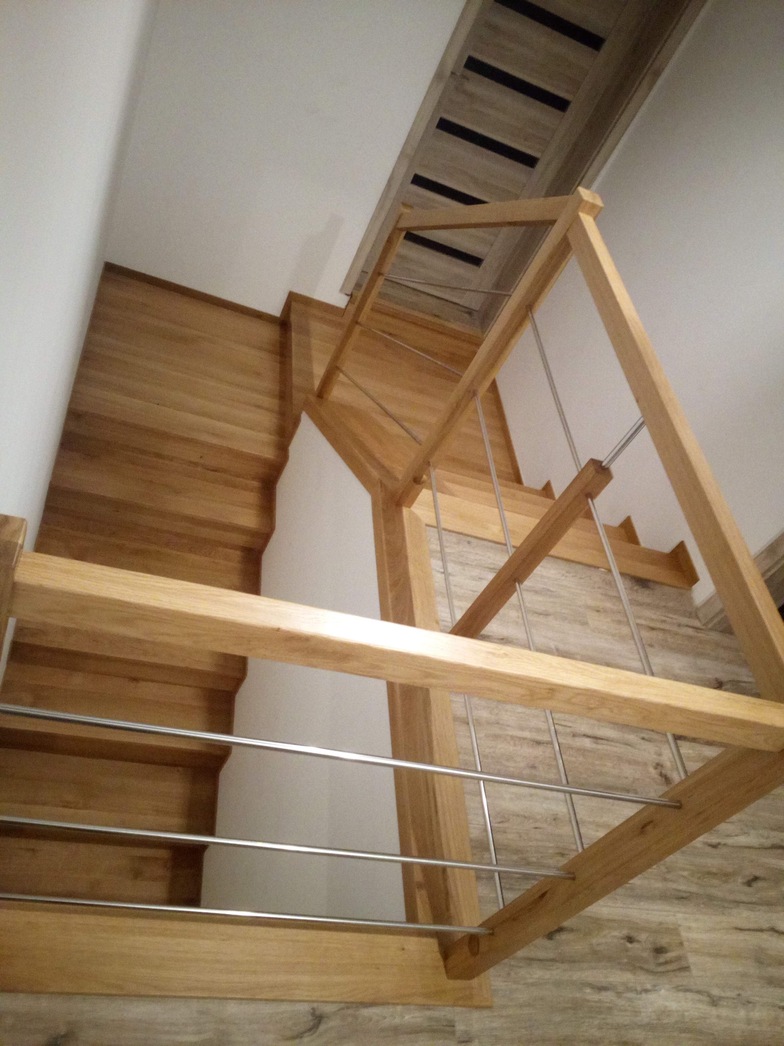 Nowoczesne schody drewniane z metalowymi balustradami, widok z dołu, jasne drewno, minimalistyczny design.