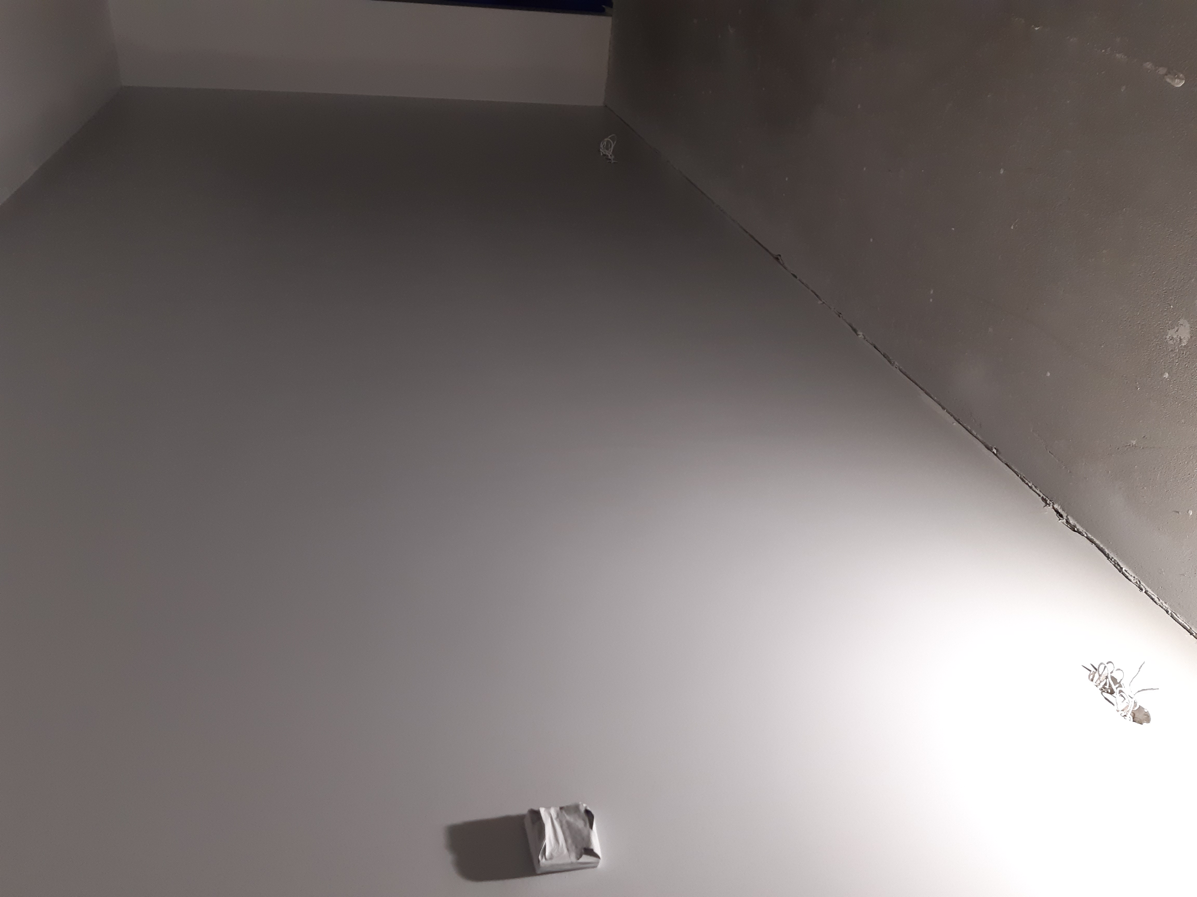 Fragment wnętrza w trakcie prac wykończeniowych, widoczna świeżo pomalowana ściana z wystającymi kablami elektrycznymi i zabezpieczonym gniazdkiem, surowy strop, przygotowywane do dalszych prac.