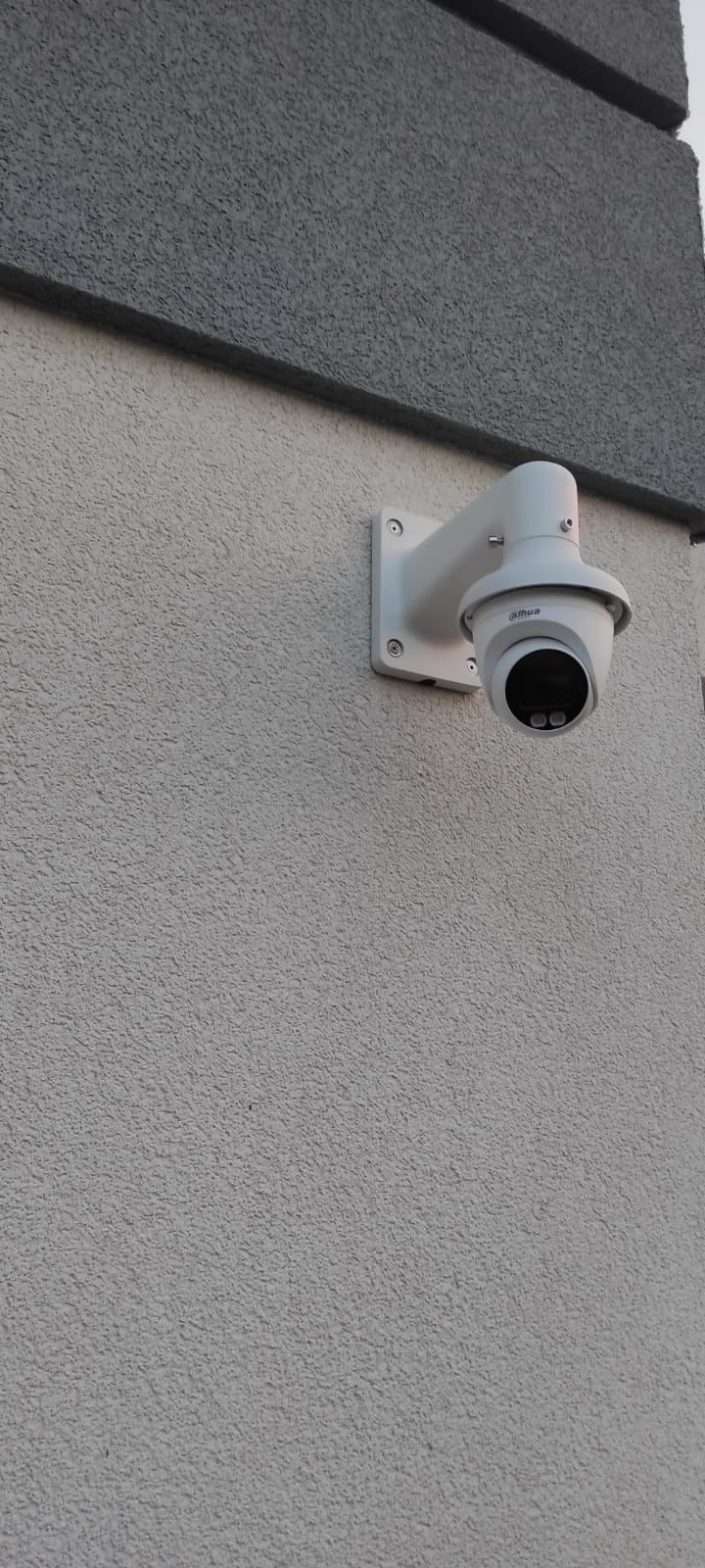 Kamera IP Dahua zamontowana na elewacji budynku o jasnoszarej strukturze, widok z dołu pod kątem.