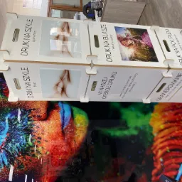 Ekspozycja wzorów druku na szkle, blasze i PCV, prezentująca różnorodne tekstury i grafiki, w tym abstrakcyjne wzory i portret, z widocznymi napisami informacyjnymi.