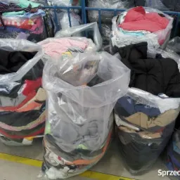 Worki foliowe wypełnione różnorodną odzieżą używaną, widoczne warstwy tkanin w różnych kolorach i wzorach, ustawione w magazynie lub hurtowni.