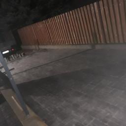 Bruk and Crash - Ułożona kostka brukowa w odcieniach szarości, oświetlona nocą, z widocznym fragmentem drewnianego ogrodzenia w tle.