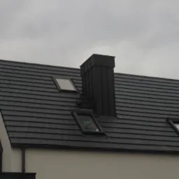 Czarny dach z dachówki ceramicznej z trzema oknami dachowymi i kominem w nowoczesnym domu pod pochmurnym niebem.