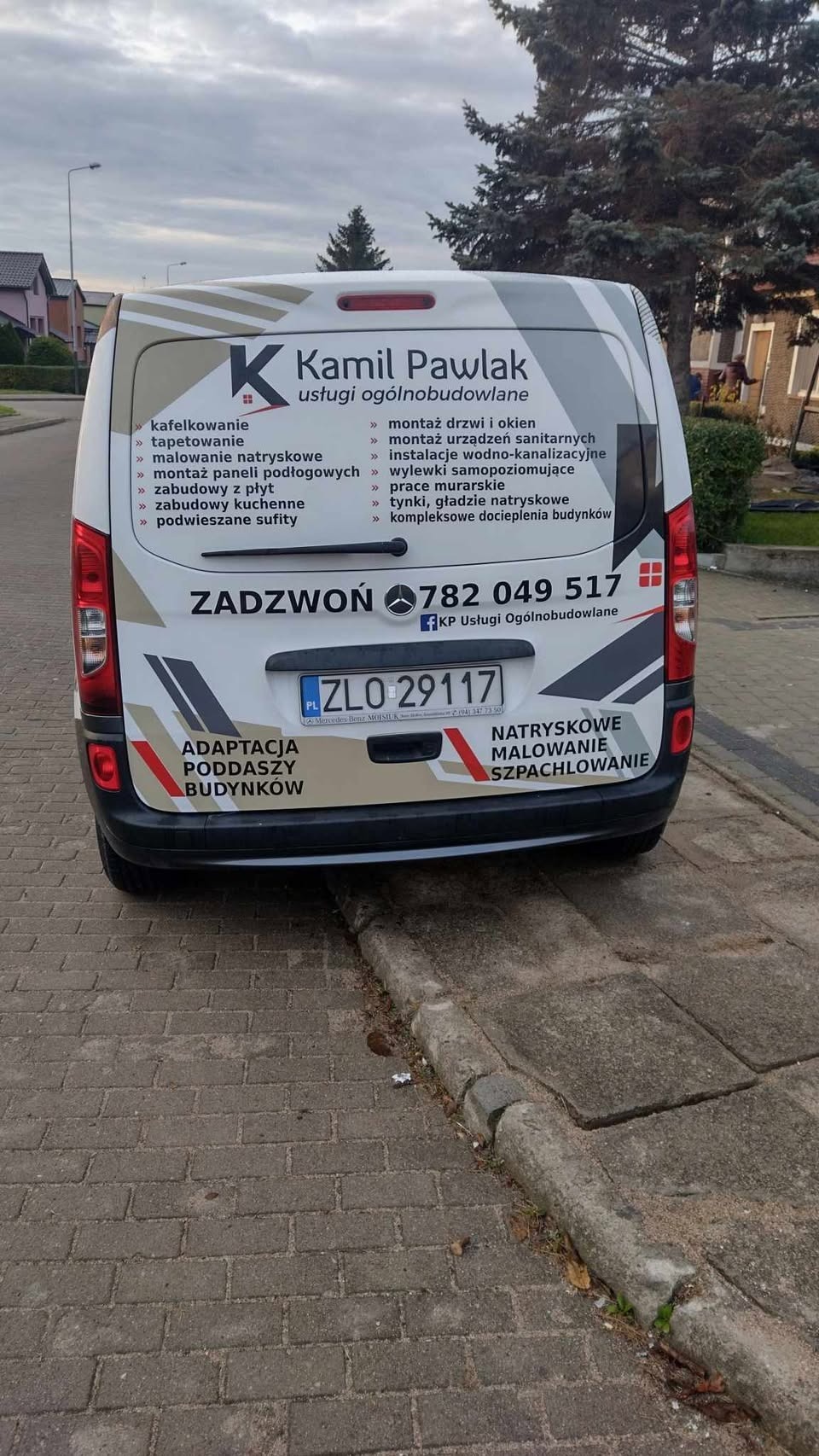 Tył samochodu dostawczego z reklamą usług ogólnobudowlanych firmy Kamil Pawlak, zawierającą spis oferowanych prac i numer telefonu, zaparkowanego na brukowanej ulicy.
