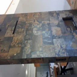 Blat kuchenny z płytek imitujących kamień naturalny, z wpuszczonym gniazdkiem elektrycznym i oświetleniem, widok z dołu na tle jasnego pomieszczenia.