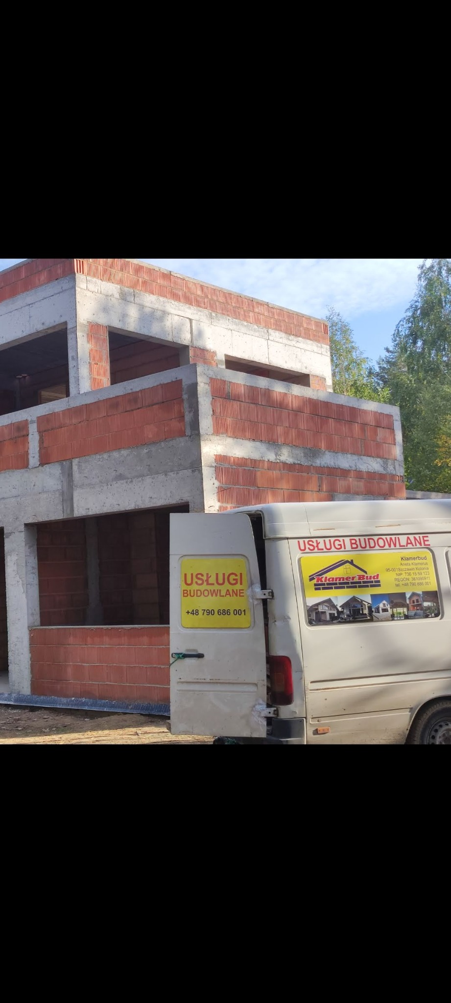 Wznoszony dom murowany z betonu komórkowego i czerwonej cegły, widok z boku z zaparkowanym białym vanem z reklamą usług budowlanych.
