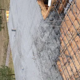 Świeżo wylany beton na deskowaniu z widocznym zbrojeniem stalowym, fragment konstrukcji budynku w trakcie budowy.