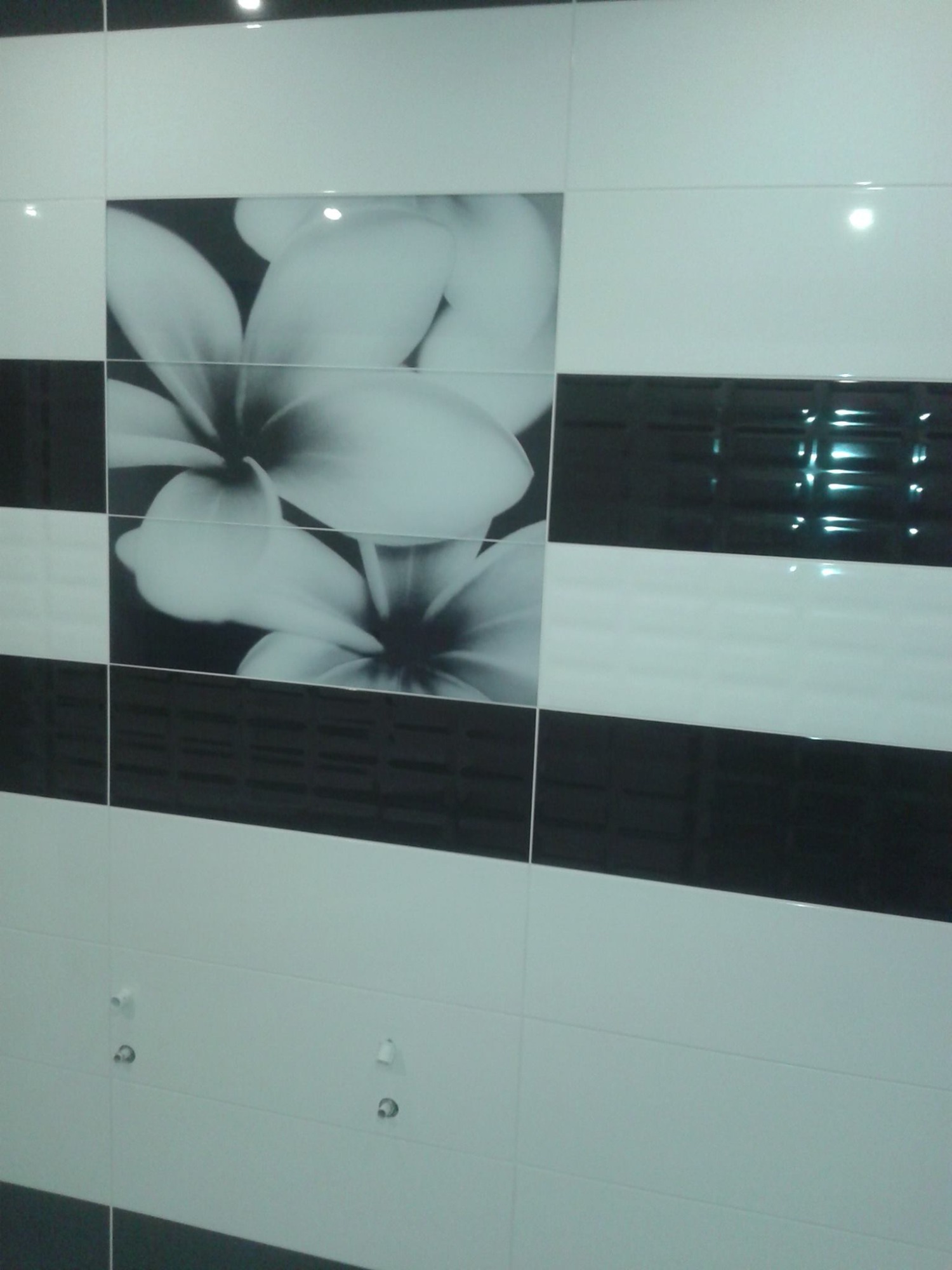 Ułożona glazura w Godziesze Małe, z motywem kwiatowym na czarno-białych płytkach, uzupełniona o czarne, błyszczące pasy i przygotowane przyłącza hydrauliczne.