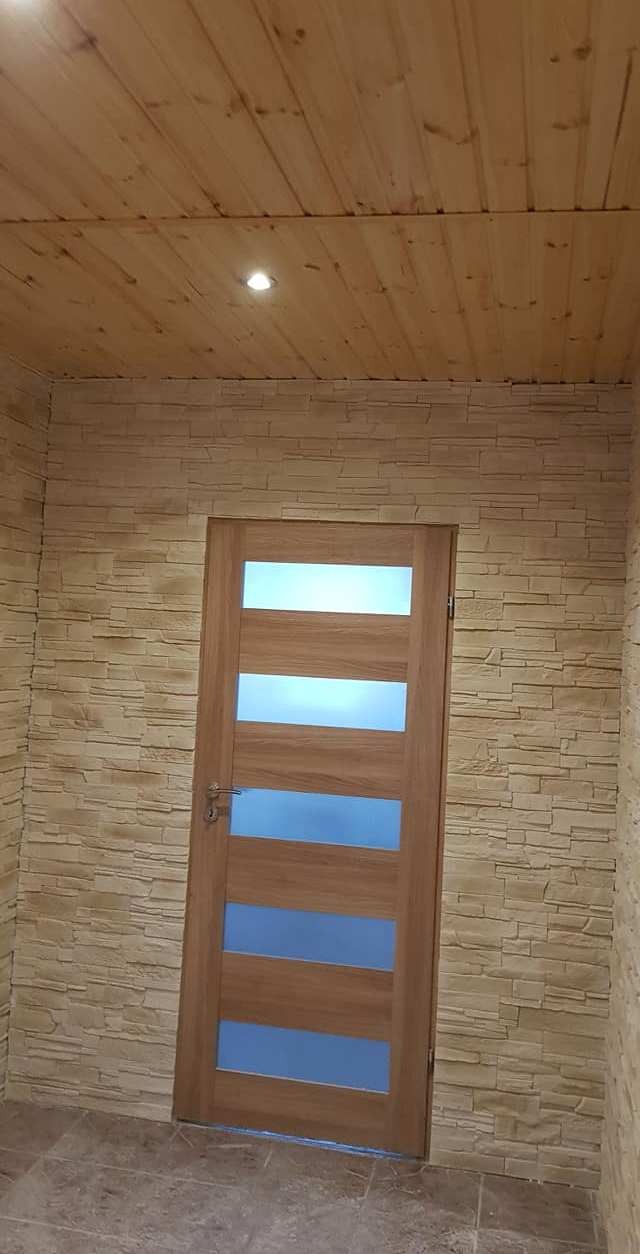 Wnętrze wykończone panelami imitującymi kamień, z drewnianym sufitem i drzwiami z przeszkleniami w kolorze niebieskim.