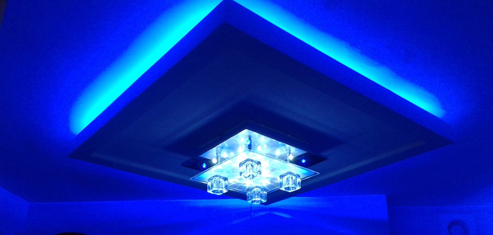 Nowoczesny sufit podwieszany z oświetleniem LED w odcieniach niebieskiego, centralnie umieszczony kryształowy żyrandol