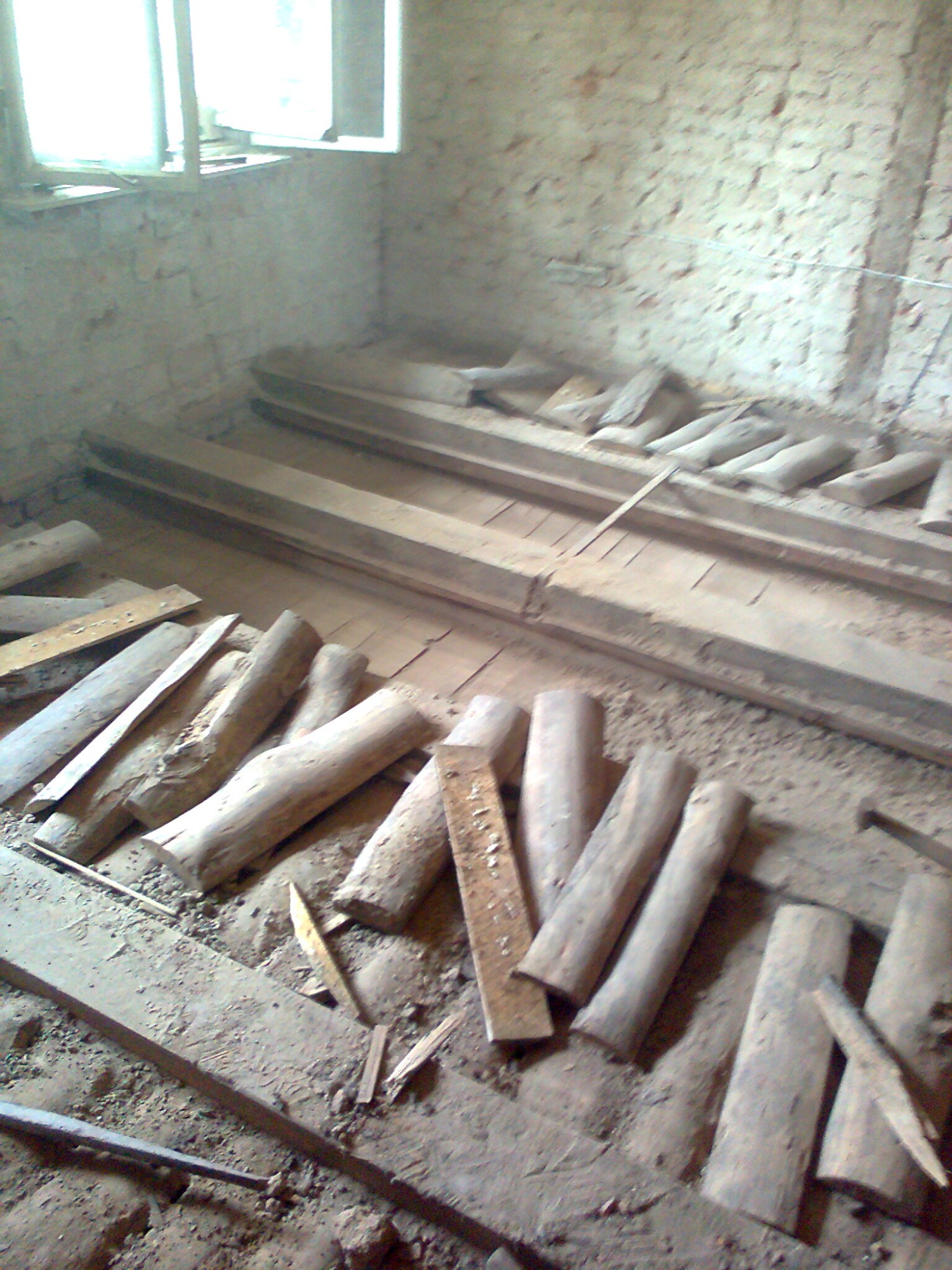 Surowe drewniane legary i deski podłogowe w trakcie przygotowania pod nowy parkiet w pomieszczeniu z oknem i surowymi ścianami.