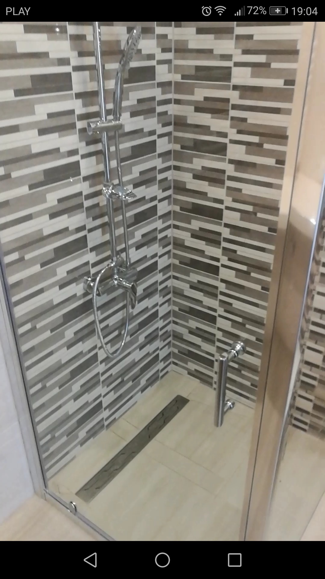 Kabina prysznicowa z odpływem liniowym, wyłożona płytkami w odcieniach szarości i beżu ułożonymi w poziome pasy.