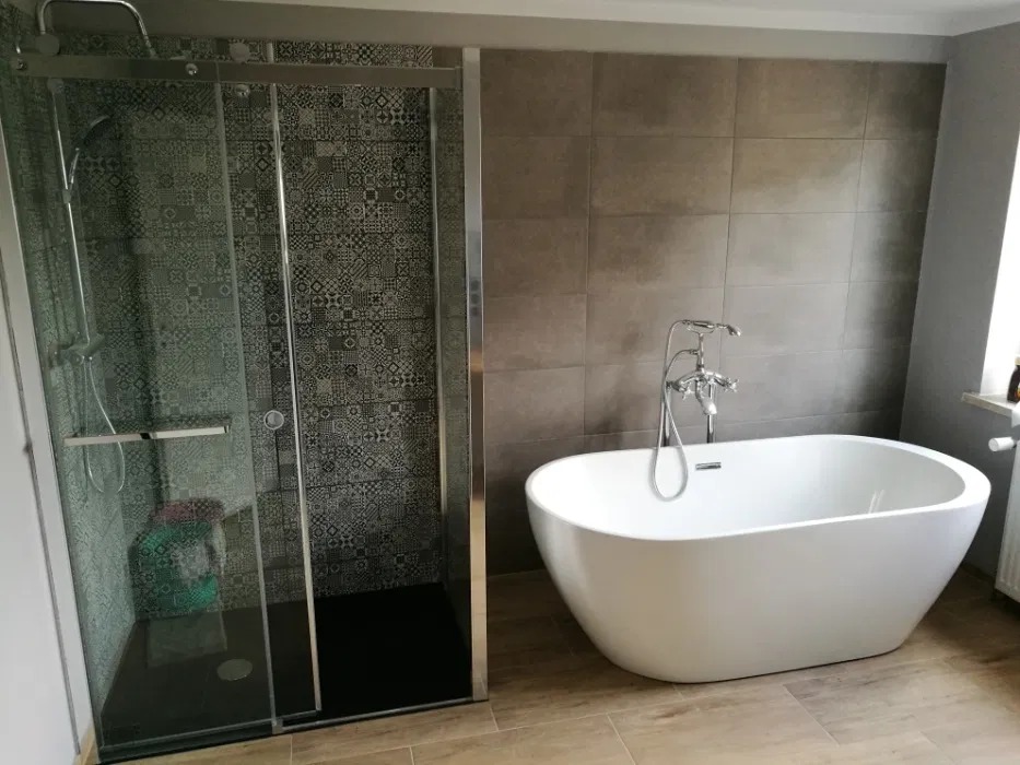 Nowoczesna łazienka z kabiną prysznicową z wzorzystymi płytkami i wolnostojącą białą wanną z chromowaną baterią.