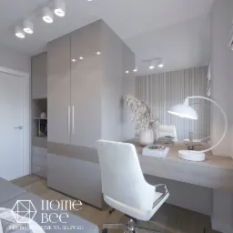 Nowoczesne biuro domowe w odcieniach szarości, z minimalistyczną szafą w zabudowie, biurkiem z dekoracjami, białym krzesłem obrotowym i lampą biurkową. Widoczny fragment sofy z logo firmy Home Bee.