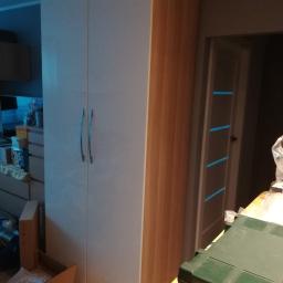 Forma drewna - Dwudrzwiowa szafa z białymi frontami i bokami imitującymi drewno, widoczna w trakcie montażu, z narzędziami Metabo w zielonej skrzynce na pierwszym planie.