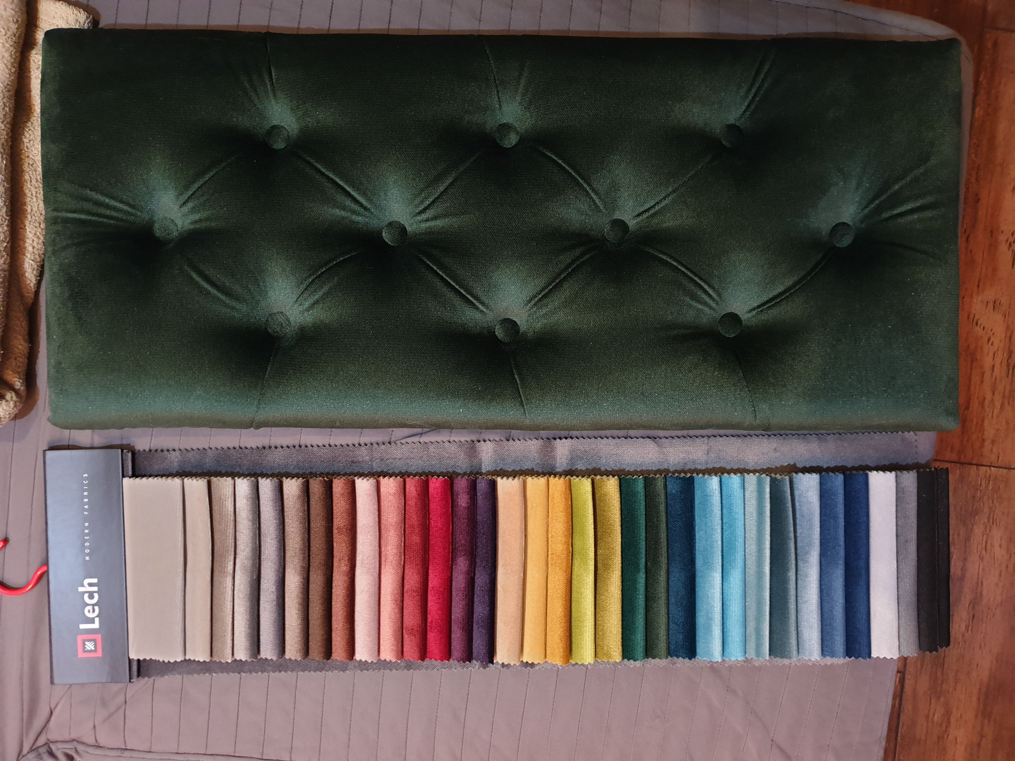 Próbnik tkanin firmy Lech z paletą kolorystyczną obok fragmentu ciemnozielonego panelu tapicerowanego z pikowaniem w romby.