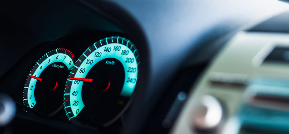 Podświetlony, niebiesko-zielony zestaw wskaźników samochodowych: prędkościomierz wskazujący około 70 km/h i obrotomierz wskazujący 1500 obr./min.