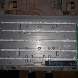 Wnętrze obudowy telewizora z widocznymi listwami LED podświetlenia matrycy oraz płytą główną, leżące na wzorzystej powierzchni.