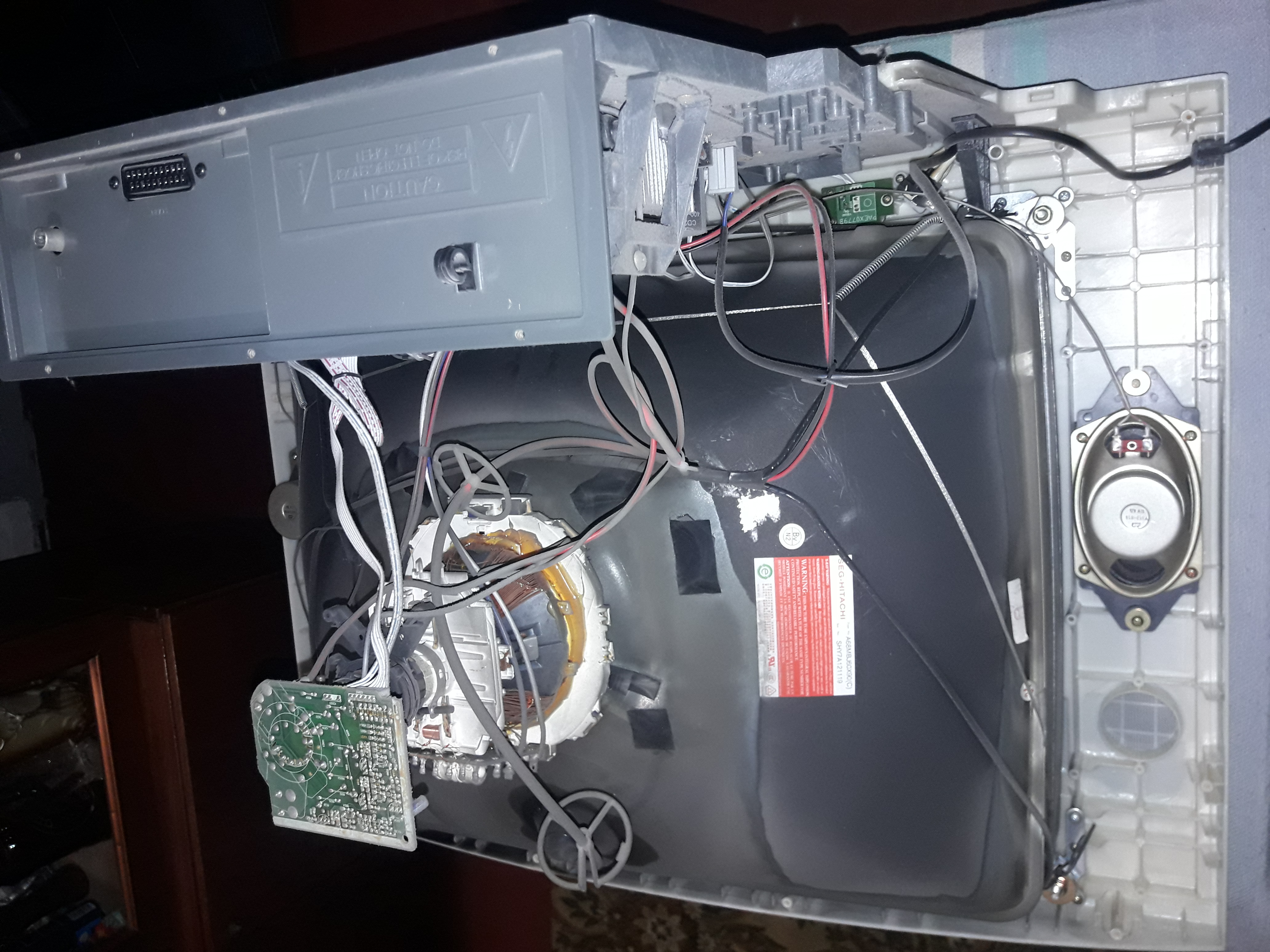 Wnętrze rozmontowanego telewizora kineskopowego z widocznymi elementami elektroniki, przewodami i głośnikiem, ukazujące proces naprawy lub demontażu.