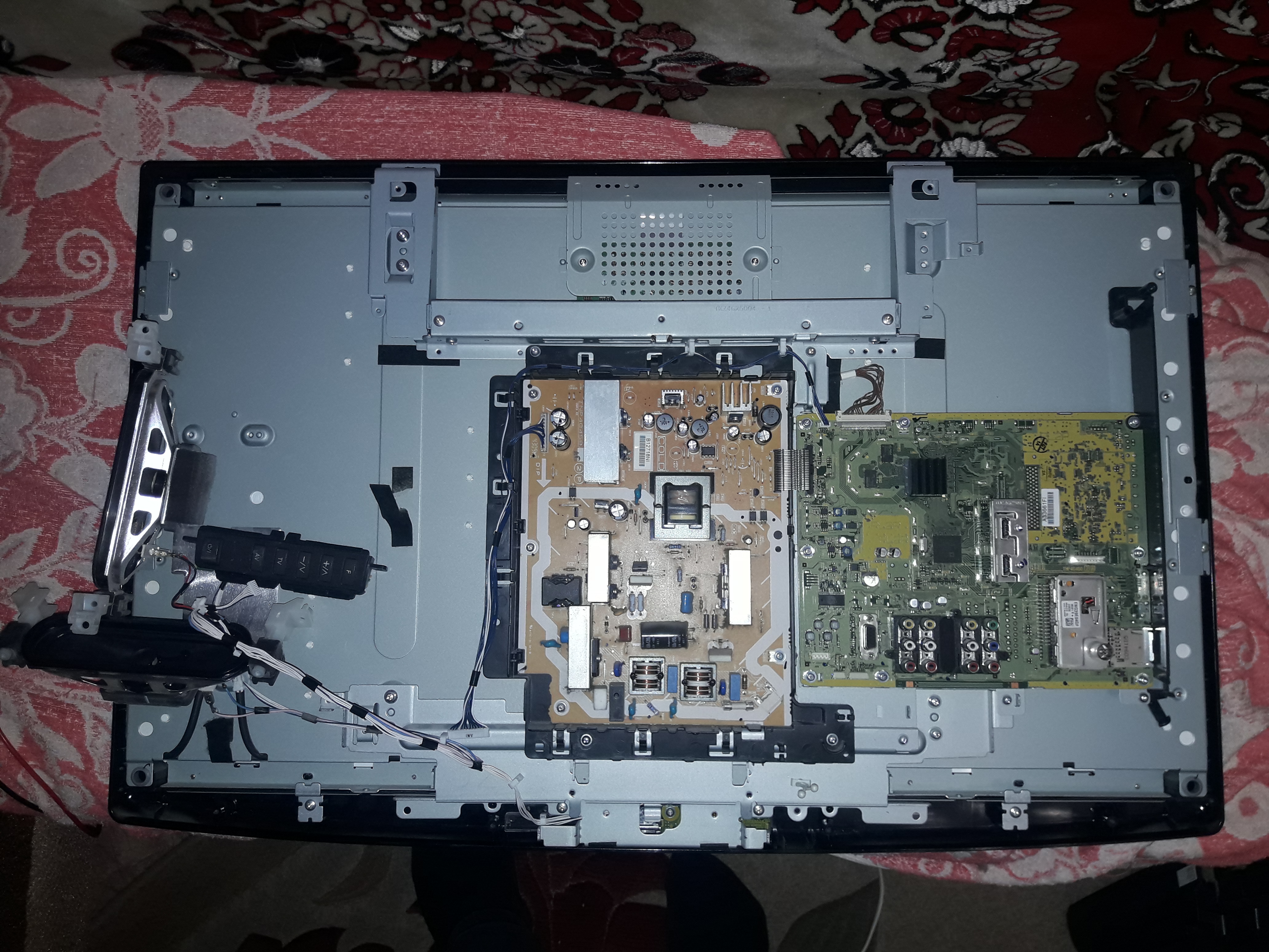 Wnętrze otwartego telewizora z widocznymi płytami głównymi i elektroniką, leżącego na wzorzystej tkaninie.