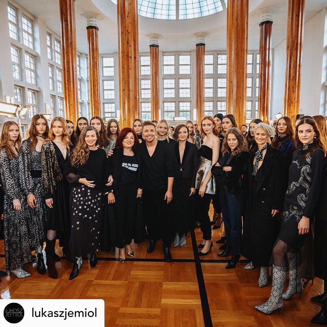 Duża grupa modelek i projektantów w Warszawie pozuje na tle kolumn w przestronnym wnętrzu, widoczne detale ubrań i makijażu.