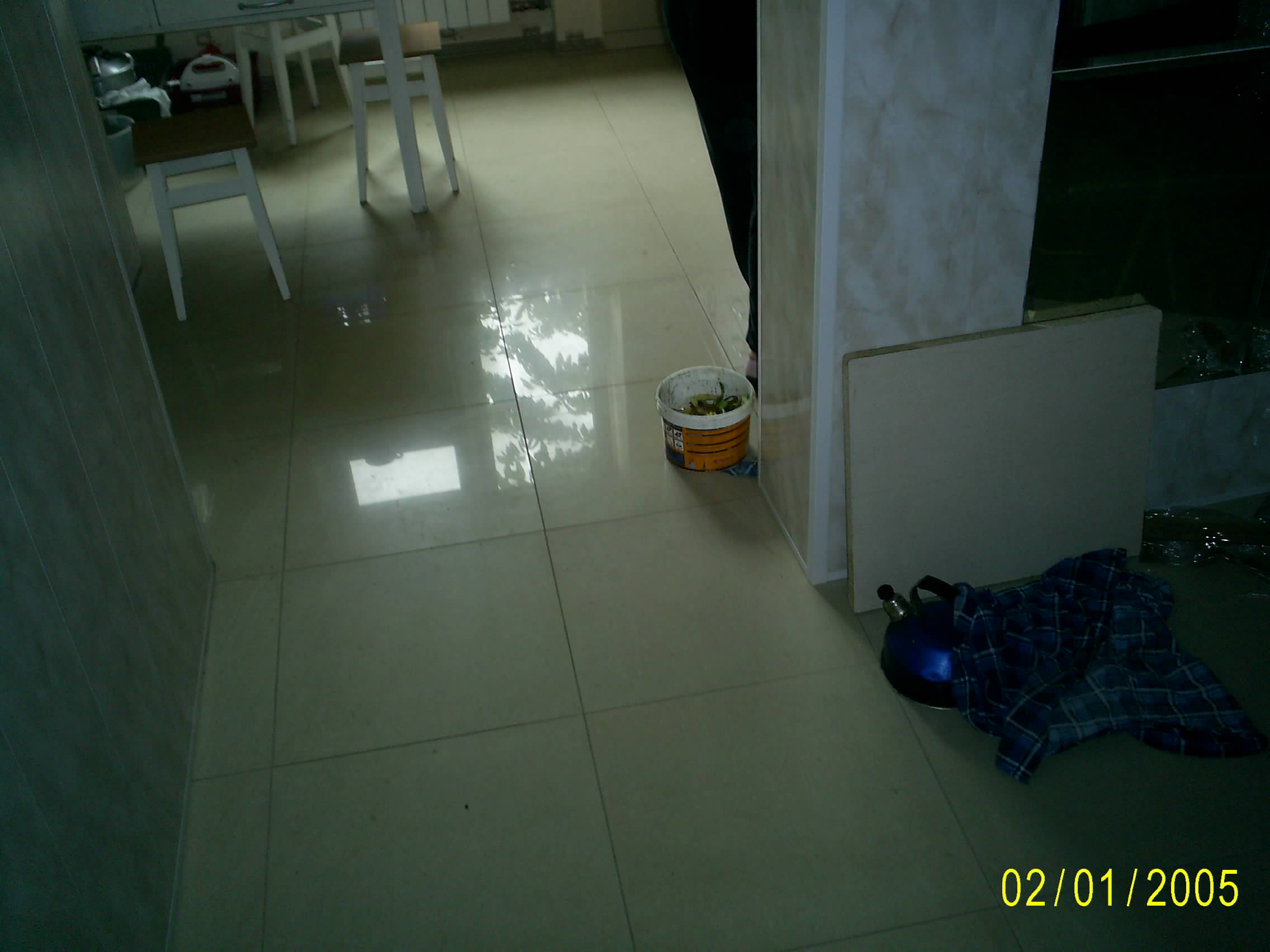 Podczas remontu: Pusta puszka po farbie z resztkami w środku stoi na błyszczącej podłodze z płytek, obok leży niebieski czajnik przykryty materiałem w kratę, w tle widoczne niedokończone elementy...