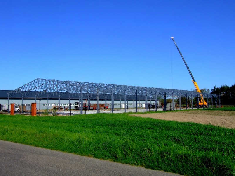 Wznoszenie stalowej konstrukcji hali w Dobre Miasto, widoczny dźwig i szkielet budynku na tle błękitnego nieba.