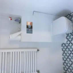 Biała, nowoczesna łazienka z wiszącą toaletą, chromowanym przyciskiem spłukiwania, grzejnikiem drabinkowym i wzorzystymi, niebiesko-zielonymi płytkami na ścianie