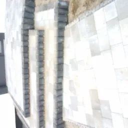 Ułożona jasnoszara kostka brukowa z ciemnoszarą obwódką, widok z góry, częściowo w cieniu budynku.