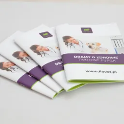 Stos czterech identycznych broszur reklamowych z wizerunkiem uśmiechniętej lekarki weterynarii i psa na okładce, z widocznym logo i adresem strony internetowej.